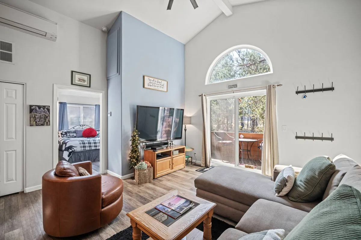 A view of the spacious living area with a large window letting in natural light, a plush sectional sofa, an entertainment center with a TV, and a wooden coffee table. The room radiates warmth and is ideal for movie marathons or relaxed gatherings.