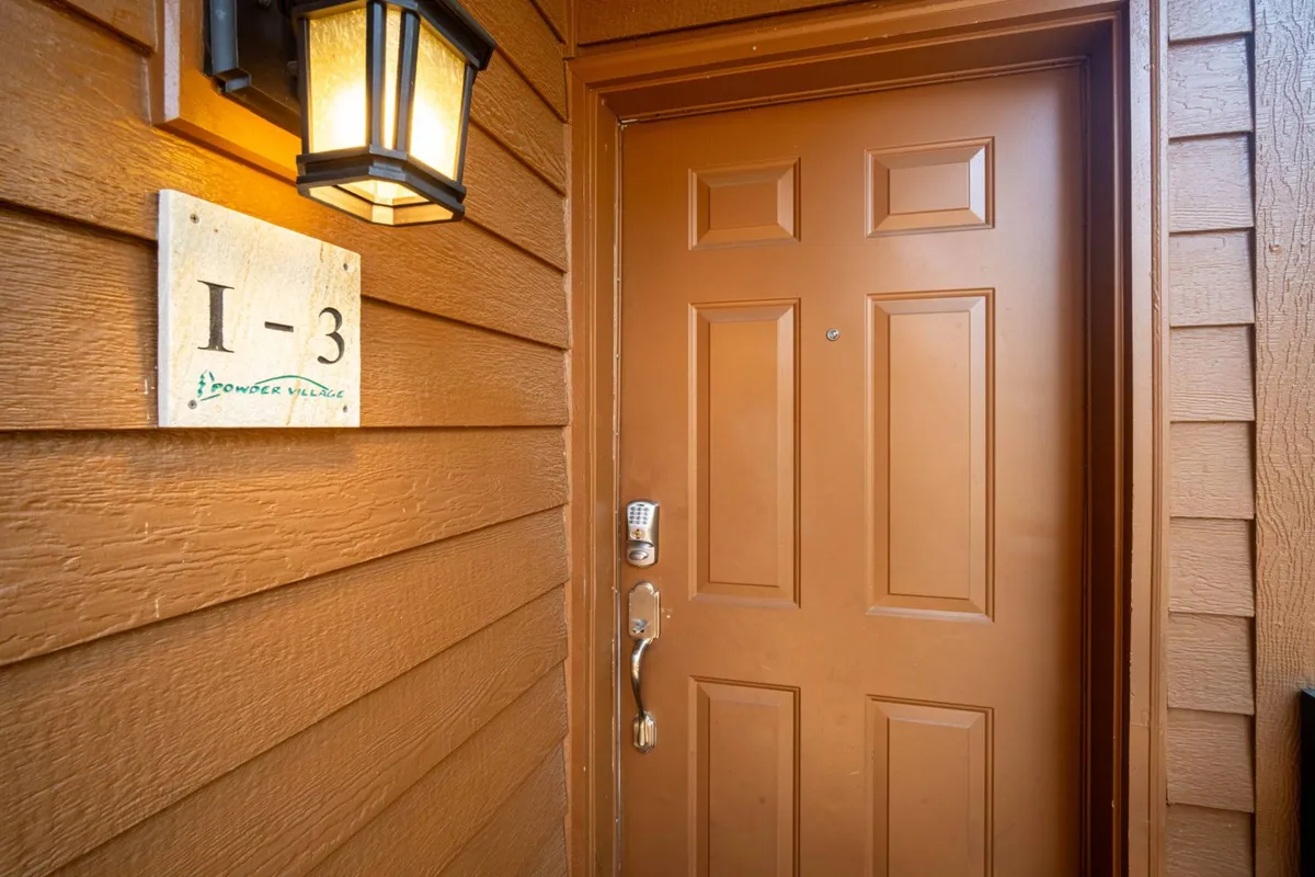 The front door of The Fisher Place is featured, with a warm, inviting light fixture and an address plaque. This close-up view suggests the start of a welcoming experience, inviting guests to step into a cozy retreat after a day of outdoor adventure.