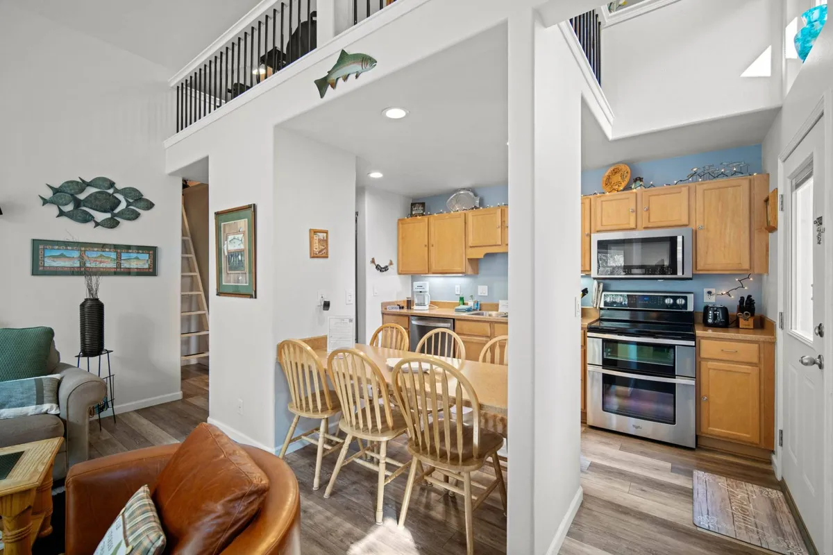 Features a wooden dining table with six matching chairs in a cozy setting, adjacent to an open kitchen. Decorative wall art and warm lighting add to the charm, making the space ideal for lingering family dinners and fun gatherings.