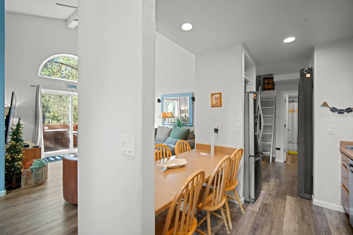 This image captures the open flow between the living area, dining table, and kitchen. The scene features a dining table set for a family meal, a comfortable couch, visible kitchen appliances, and decorative touches like plants, all basked in warm, inviting light.
