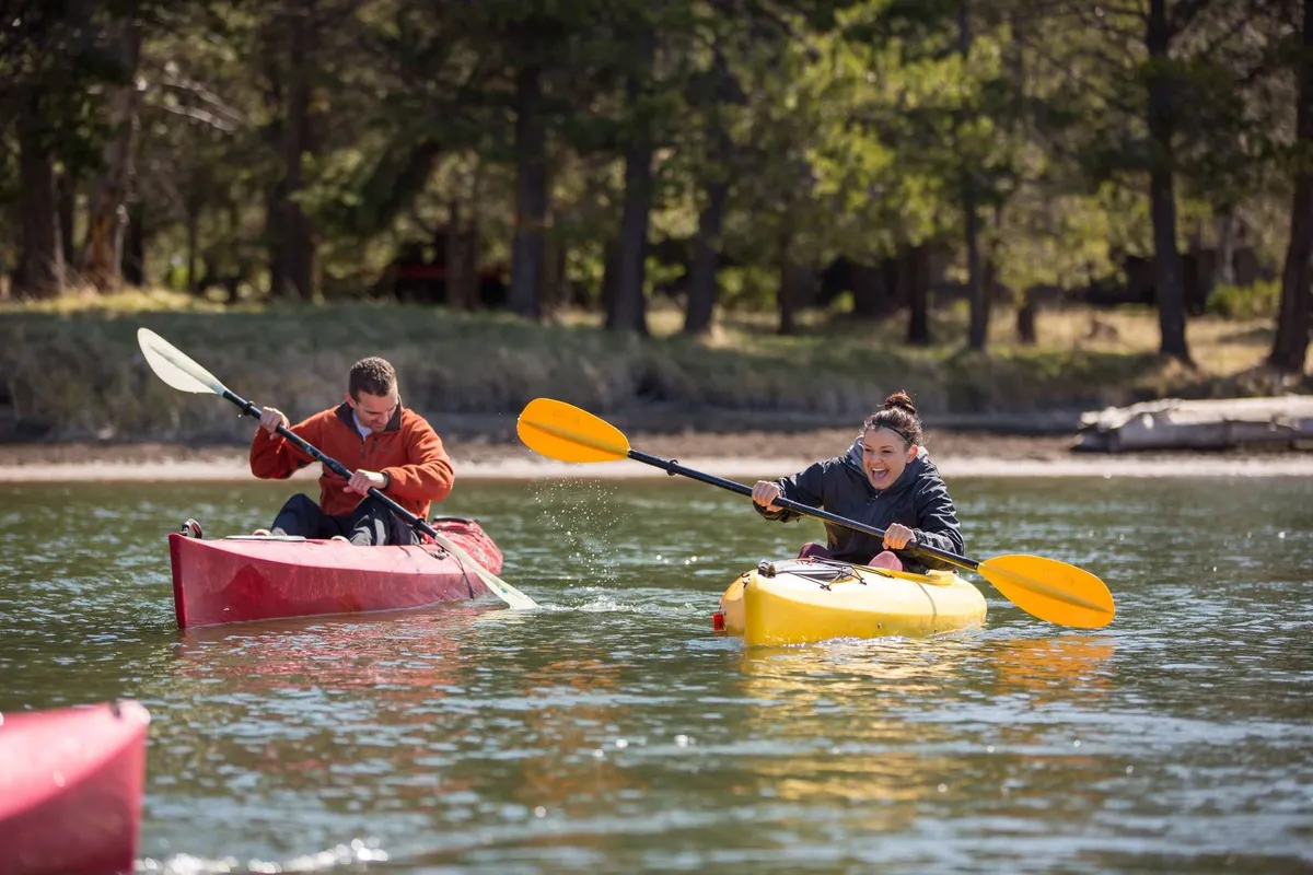 This image captures two brightly colored kayaks with participants paddling across a sparkling body of water, suggesting active outdoor fun. The water's surface glistens under natural sunlight, and the scene is lively and dynamic, evoking the spirit of adventure and togetherness.