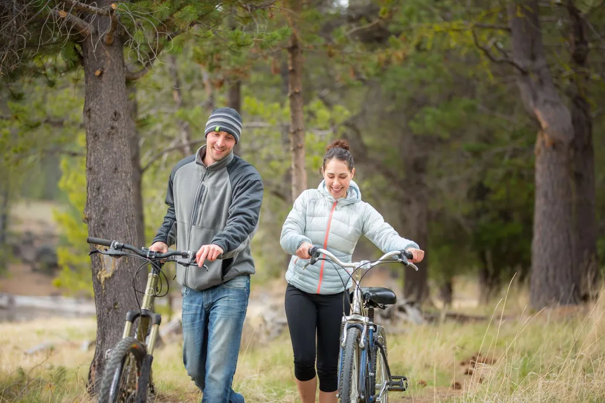 A picturesque exterior shot showing two bicycles and two people walking along a scenic, tree-lined path. The background features verdant greenery, conveying the tranquility and recreational appeal of the walking and biking trails.