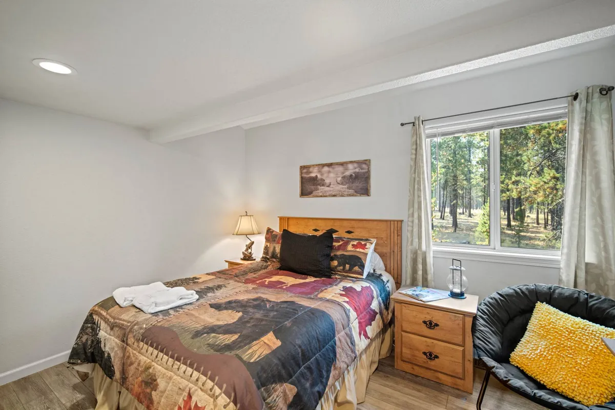 A sunlit bedroom with a decorative quilt, a comfortable bed, and a window that brings in natural light. A nightstand with a lamp and a black accent chair create a peaceful nook, perfect for reading or enjoying quiet moments after outdoor adventures.