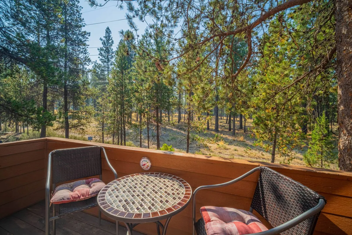 This image features a small round table and two chairs set on a balcony surrounded by tall pine trees. The setup is designed for relaxing moments, such as enjoying a morning coffee or reading a book while immersed in the tranquility of nature.