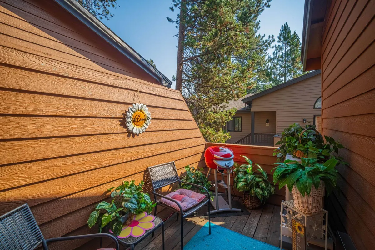A cozy exterior seating area featuring a decorative sunflower, potted plants, a comfortable seating arrangement, and a grill. This space is designed for outdoor dining, socializing, and enjoying meals al fresco just steps from home.