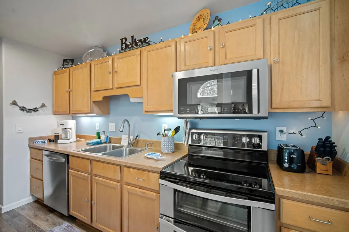 A close-up of the kitchen area featuring gleaming stainless steel appliances, wooden cabinetry, and decorative wall art. The space is designed for both culinary creativity and casual family interactions.