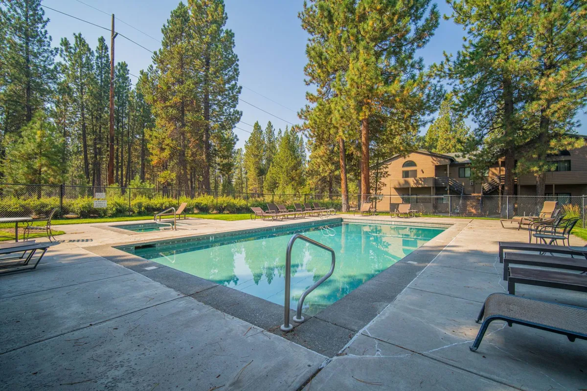 This image features an inviting swimming pool surrounded by lush trees and comfortable lounge chairs, with a relaxed, sunlit atmosphere perfect for swimming, sunbathing, and group gatherings. The pool is the central focus, enhanced by the surrounding greenery and clear sky, suggesting a laid-back resort vibe.